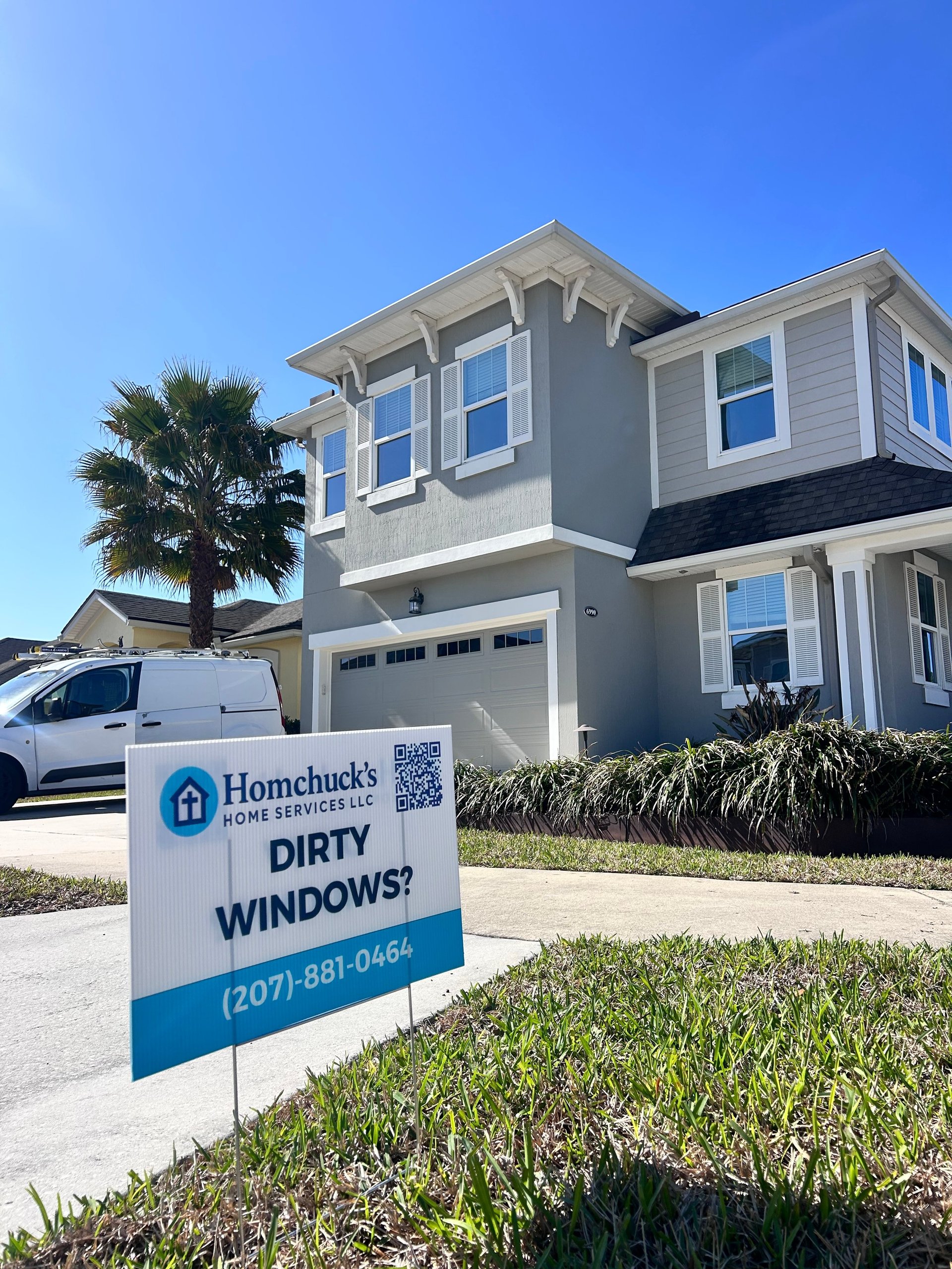 Modern two-story gray and white house with a Homchucks home services yard sign advertising dirty window cleaning services in the front lawn